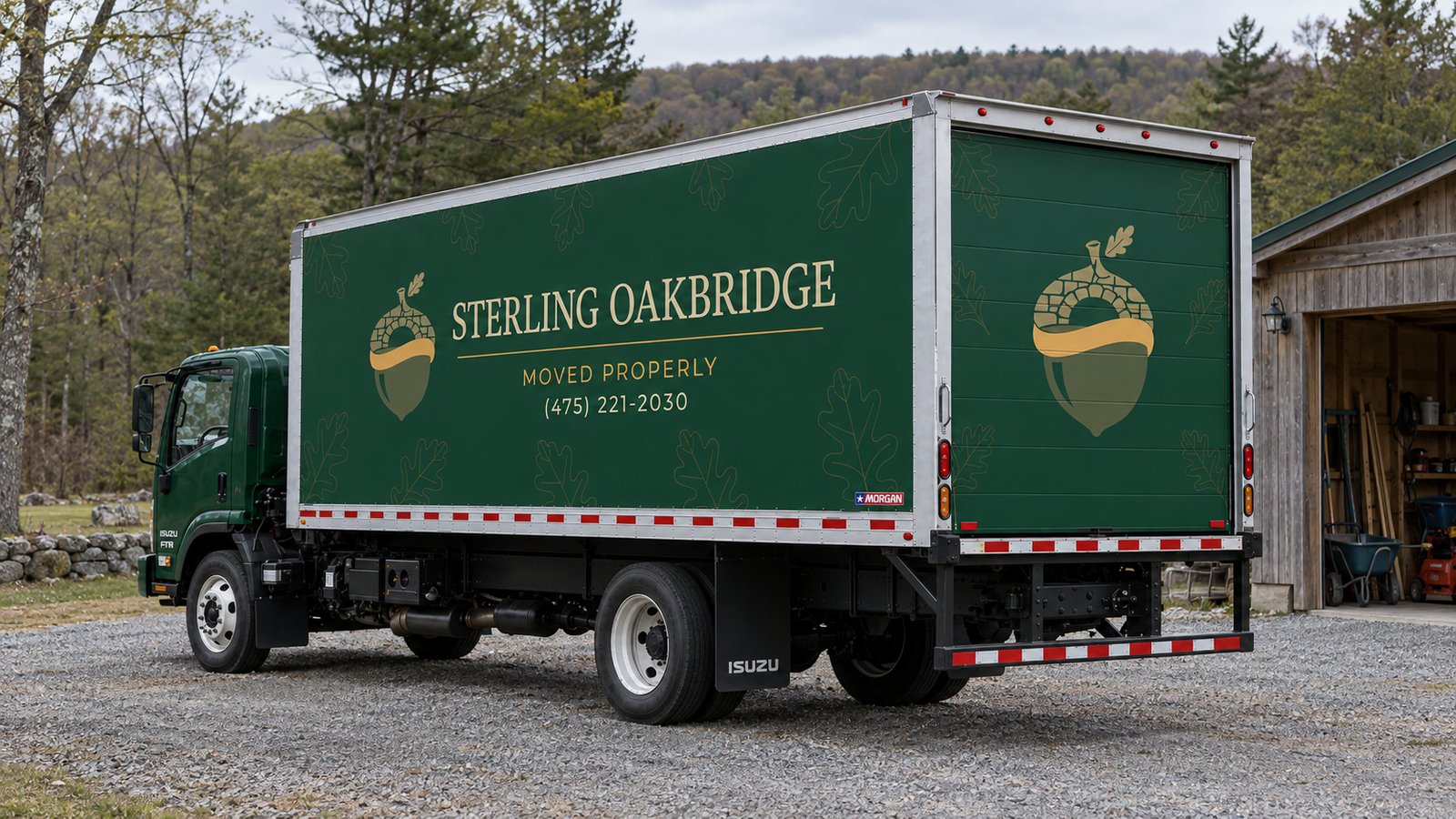 Arrange the vehicle position A complete green Sterling Oakbridge FTR26 box truck viewed from the rear quarter on a gravel apron beside a timber shed.