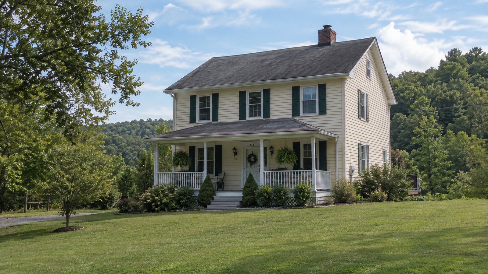 A home near wooded West Virginia hills A whole cream clapboard house with a front porch and lawn