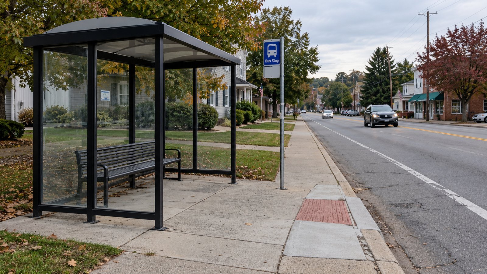 Planning the journey both ways Glass bus shelter with an empty bench beside a bus-stop sign, sidewalk and curb ramp