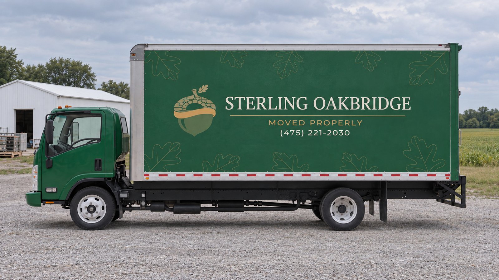 The assigned vehicle and standing space Green Sterling Oakbridge box truck parked broadside in a private gravel yard with a utility shed behind it.
