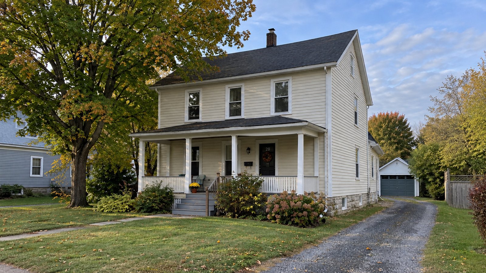A village home and its approach Cream clapboard house with covered porch, maple tree and gravel driveway