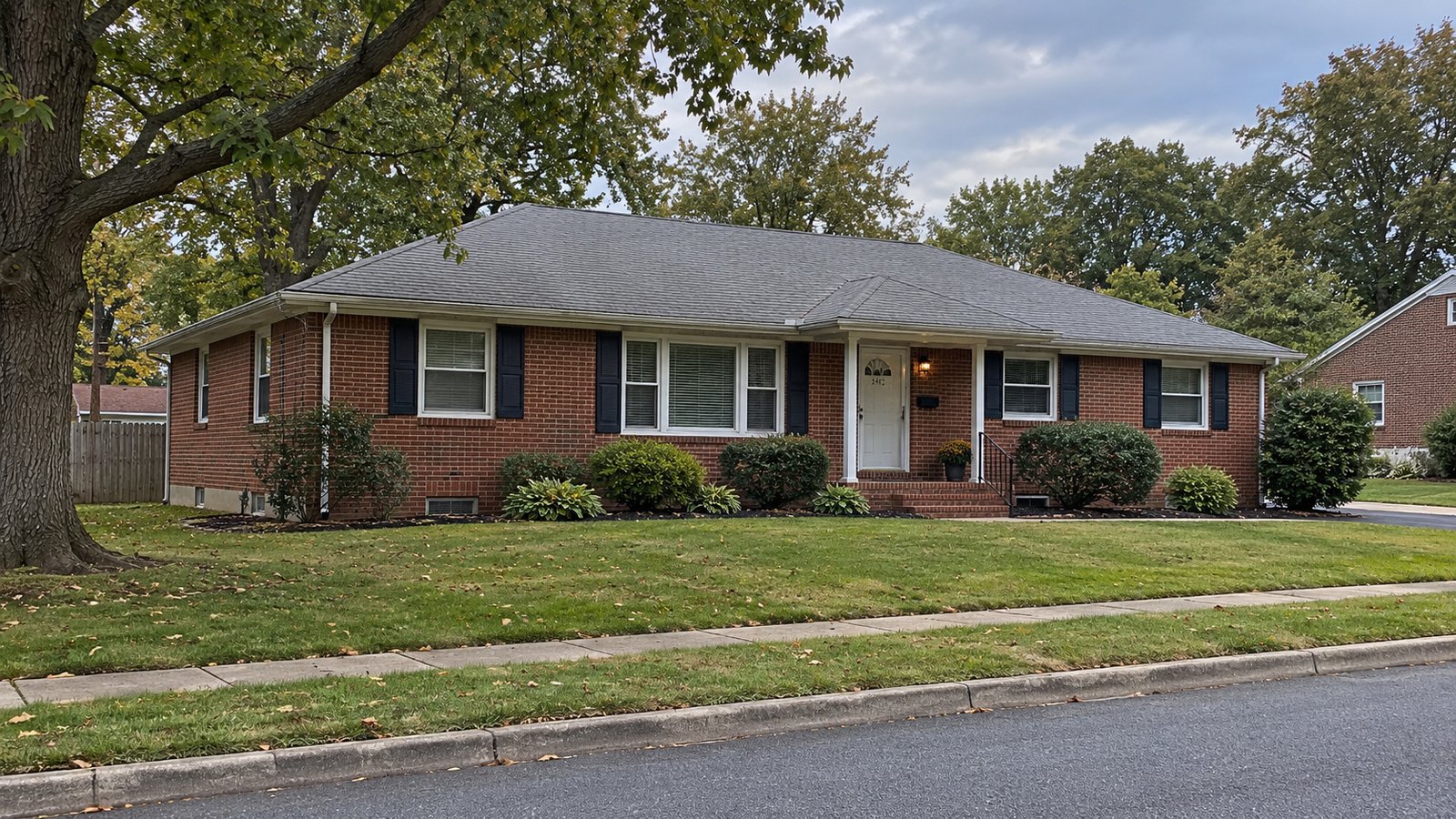 A whole red-brick ranch house with a pitched gray roof, lawn and covered entrance.