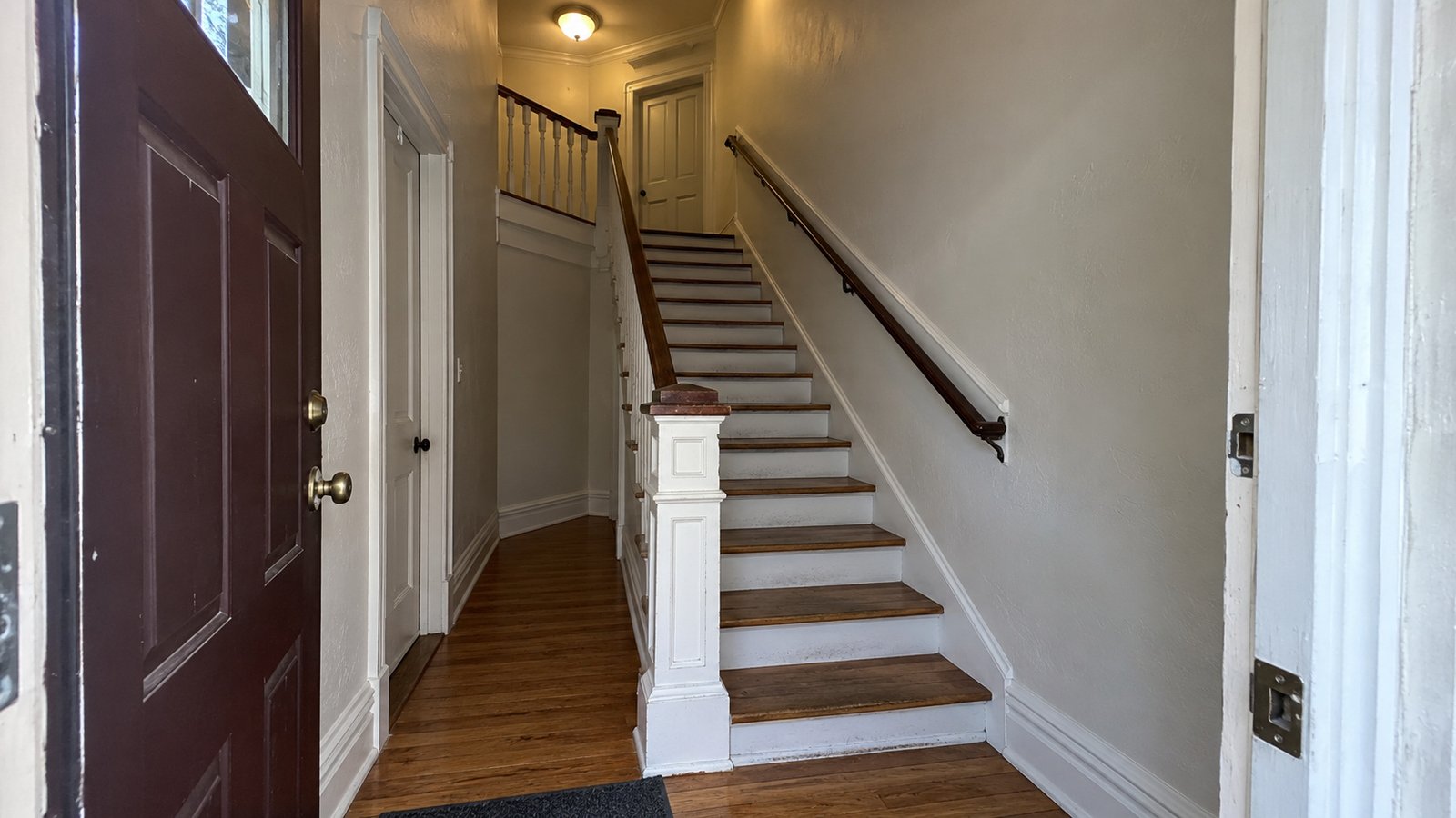 The shared stair and its turning landing An open entrance into a shared hallway, with a full wooden stair flight and an upper turning landing.