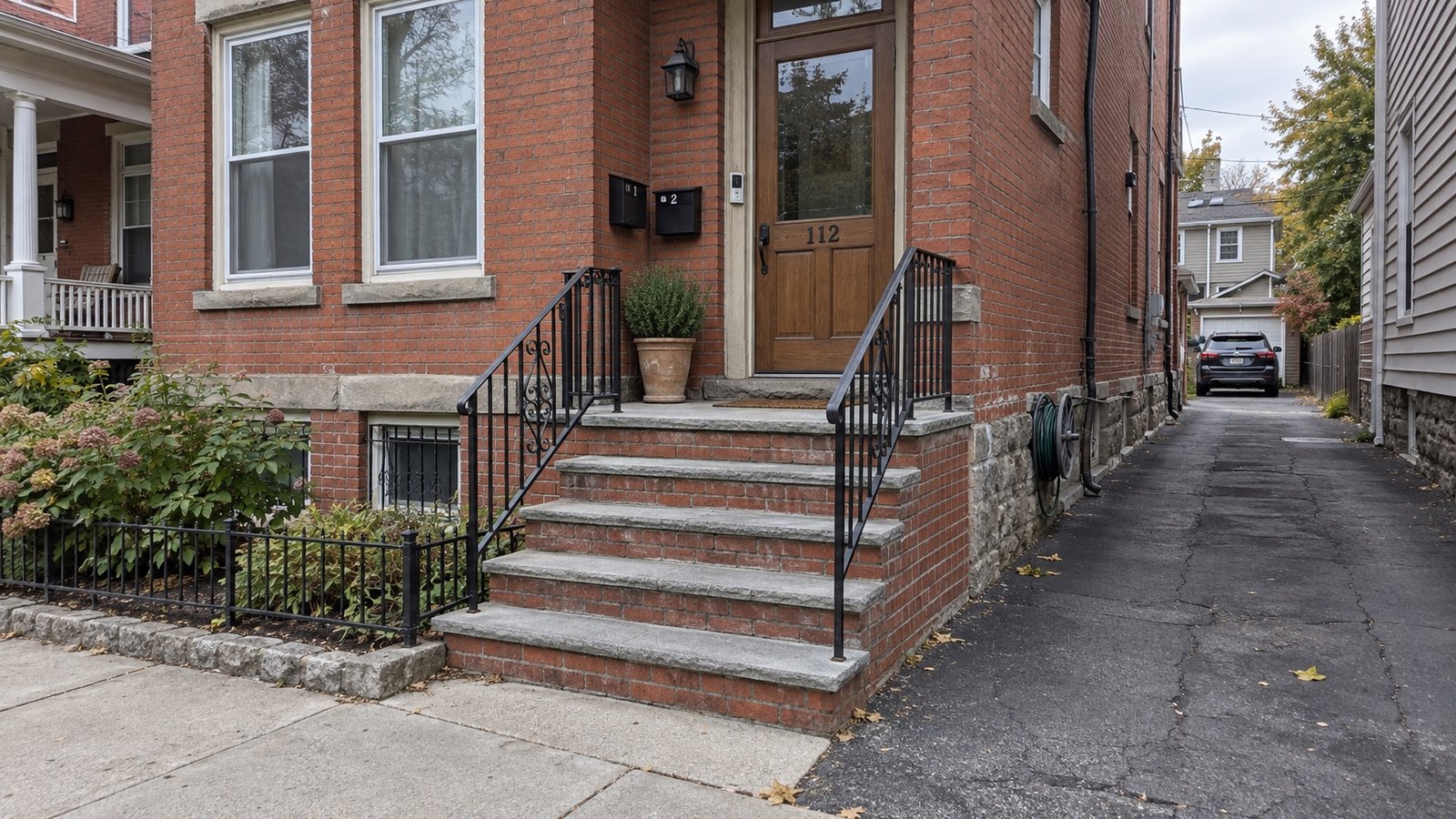 An older brick two-family house with a raised front stoop and a narrow shared driveway alongside.