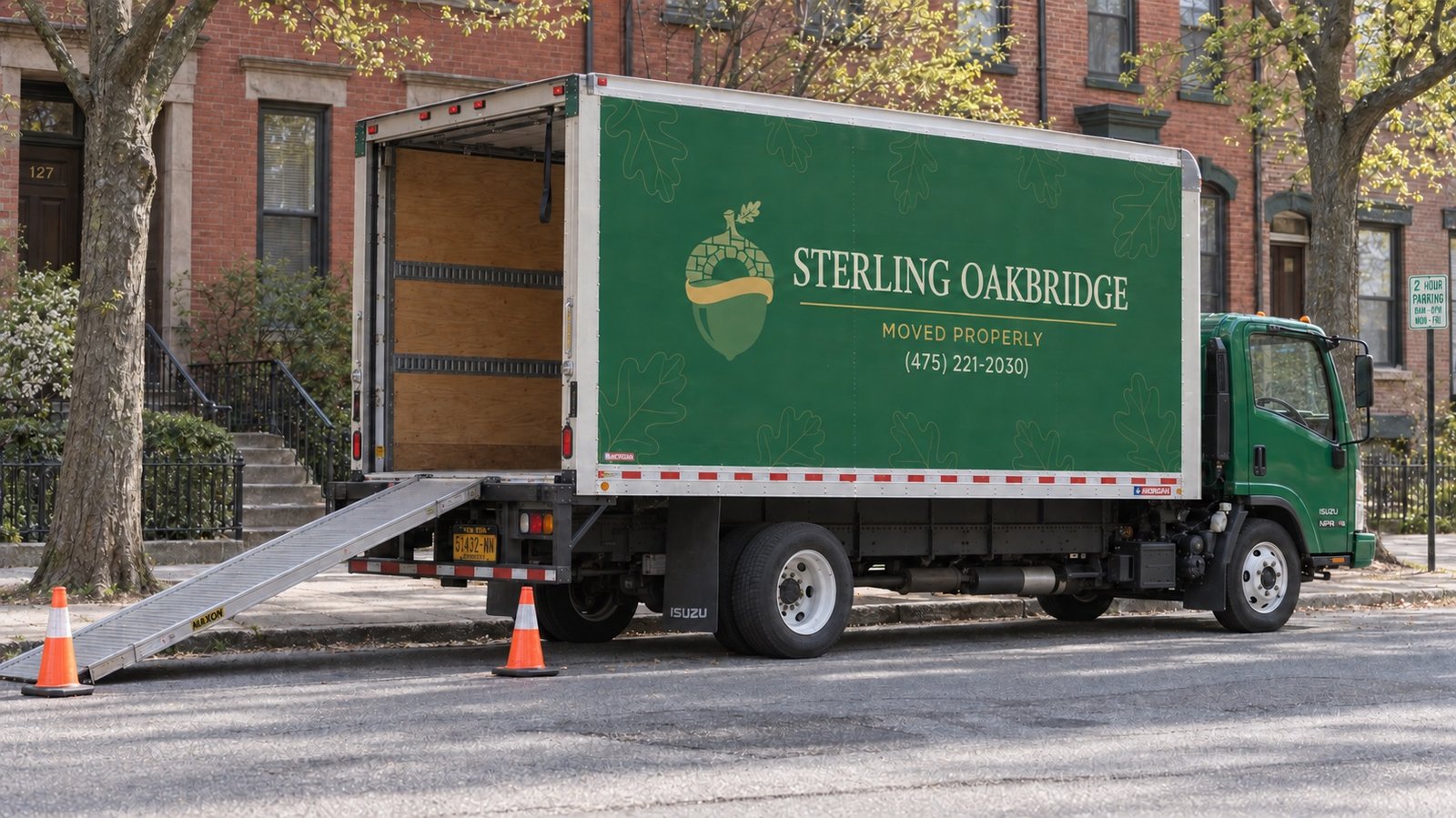 A dark green moving truck with an open rear door and a ramp resting by a residential curb.