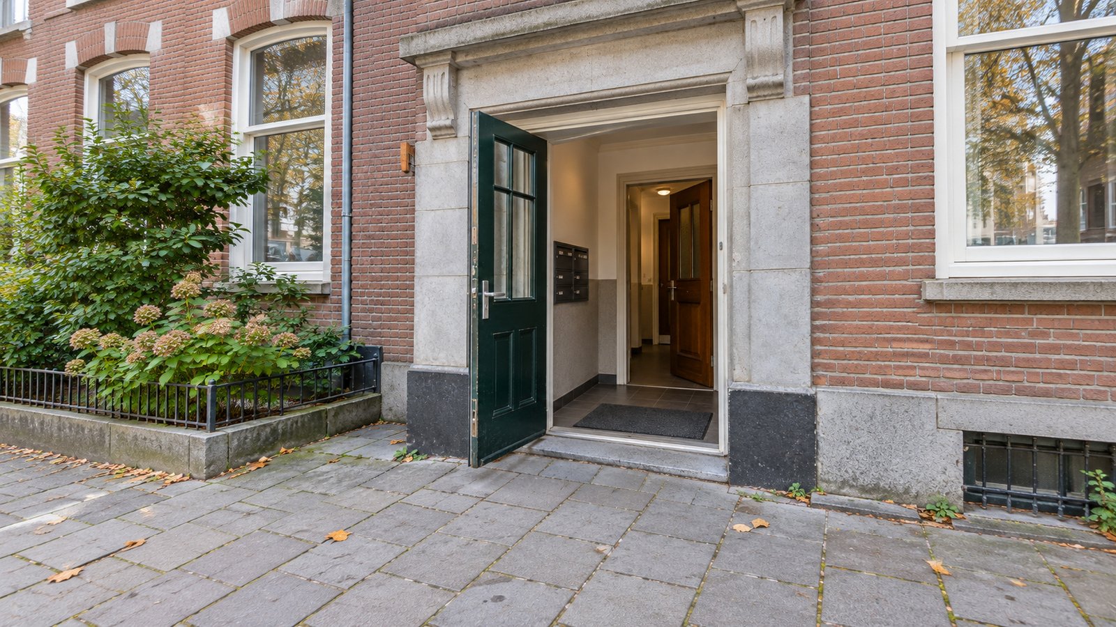 Two doorways along one carrying route Open green exterior door leading through a tiled shared vestibule to an open wooden inner door