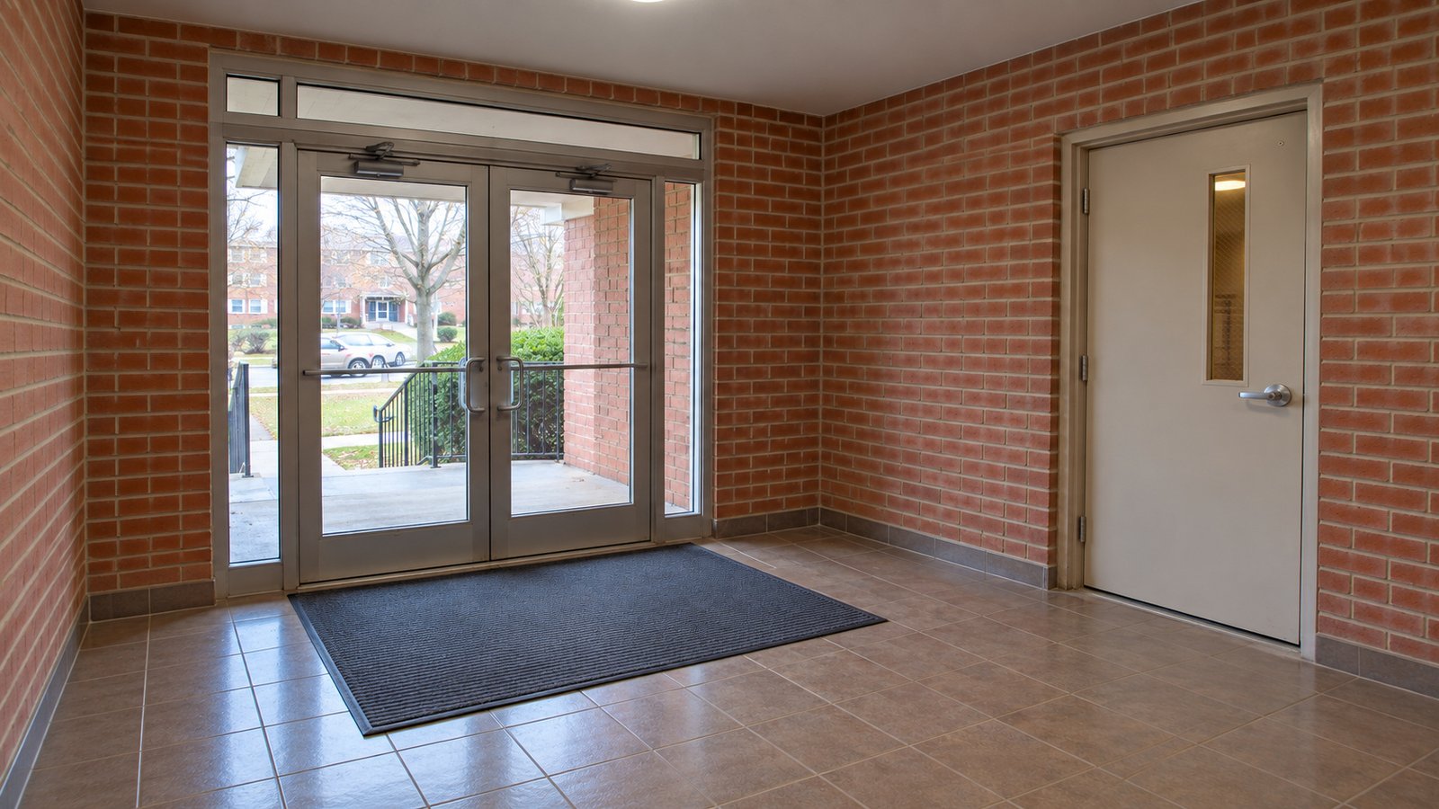Brick vestibule with double glass entrance doors, a separate inner door and a clear tiled floor