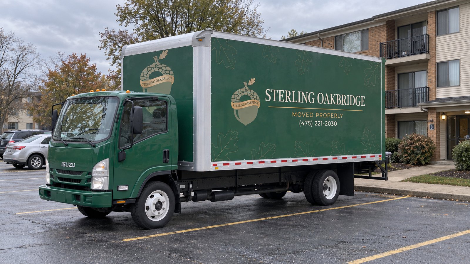Green Sterling Oakbridge cab-over box truck parked in a marked asphalt bay beside an apartment building