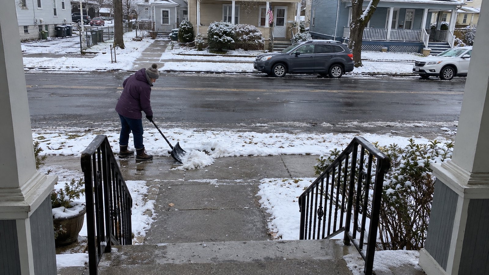 A resident shoveling a snowy sidewalk, viewed from a porch above the cleared front path.