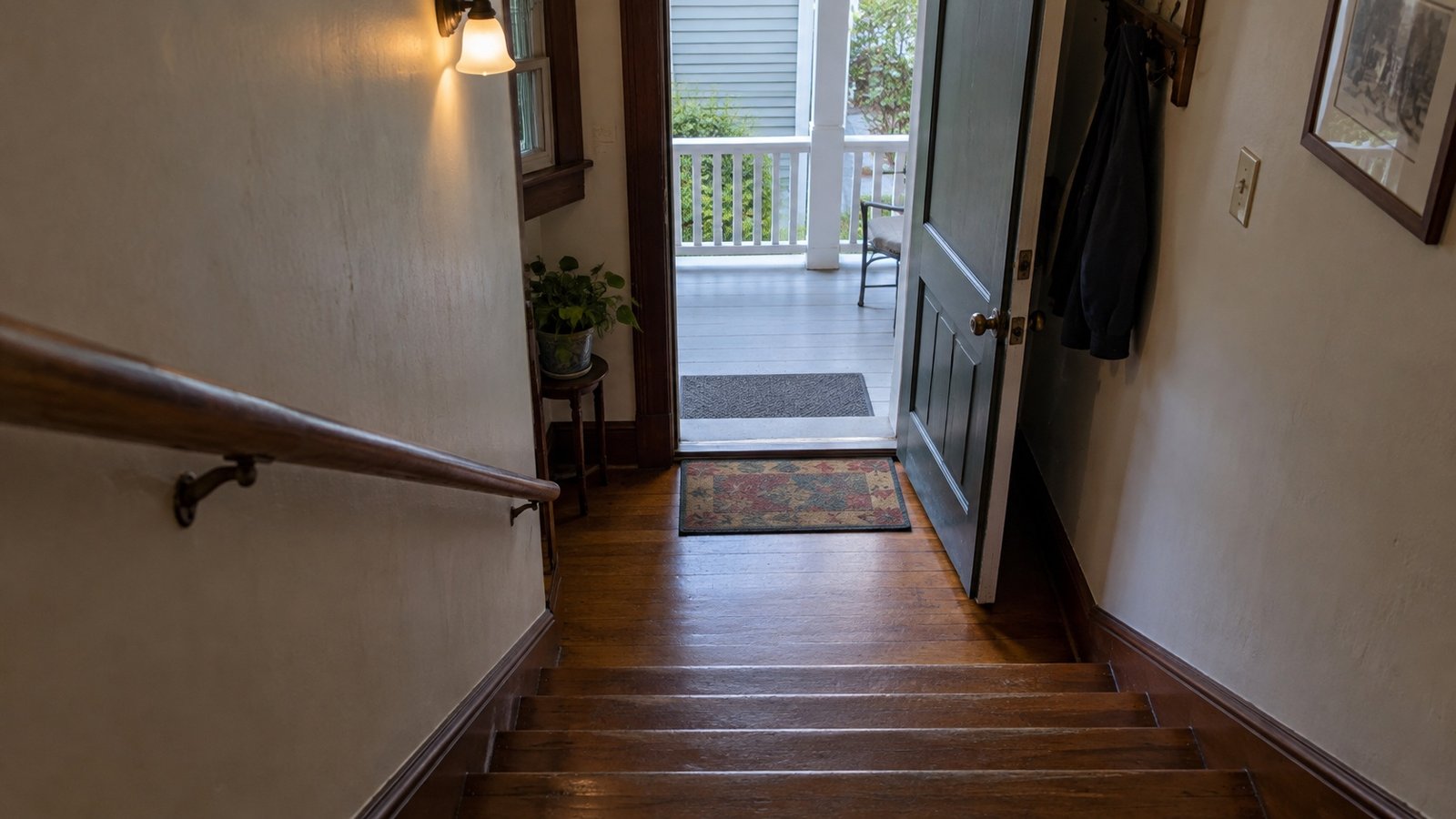 A view down wooden indoor stairs to a landing and open side door leading onto a porch.