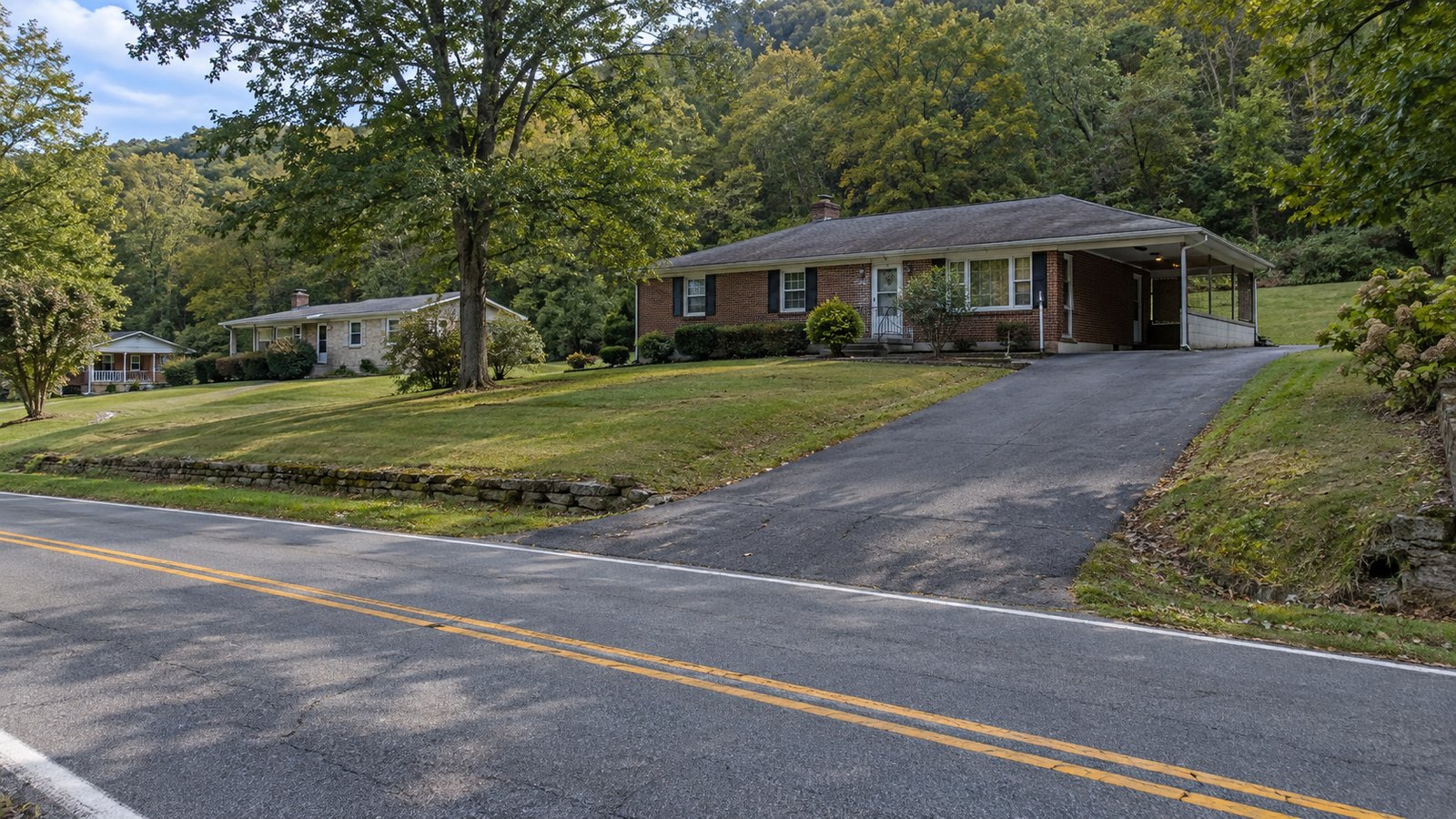 Plan the outside approach A brick ranch and carport beside a connected paved road and wooded hillside.