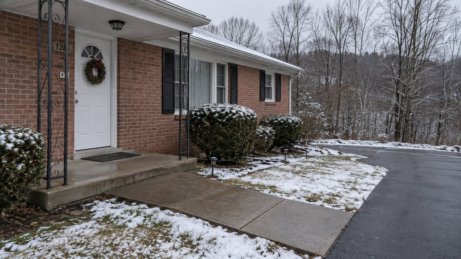 A full porch entry and cleared path beside thin snow and leafless woodland.