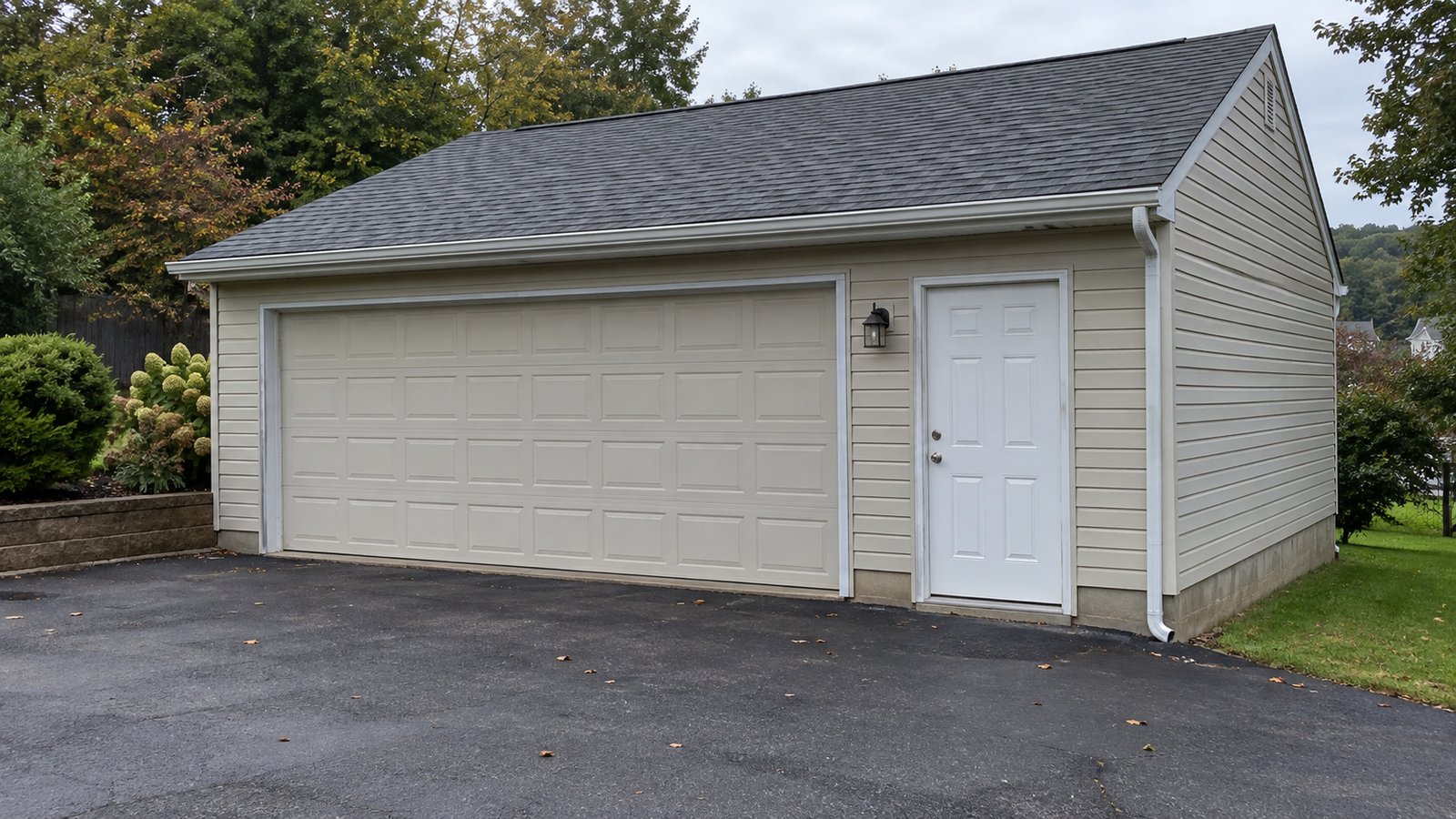 A complete cream detached garage with a closed overhead door, side door and paved apron.