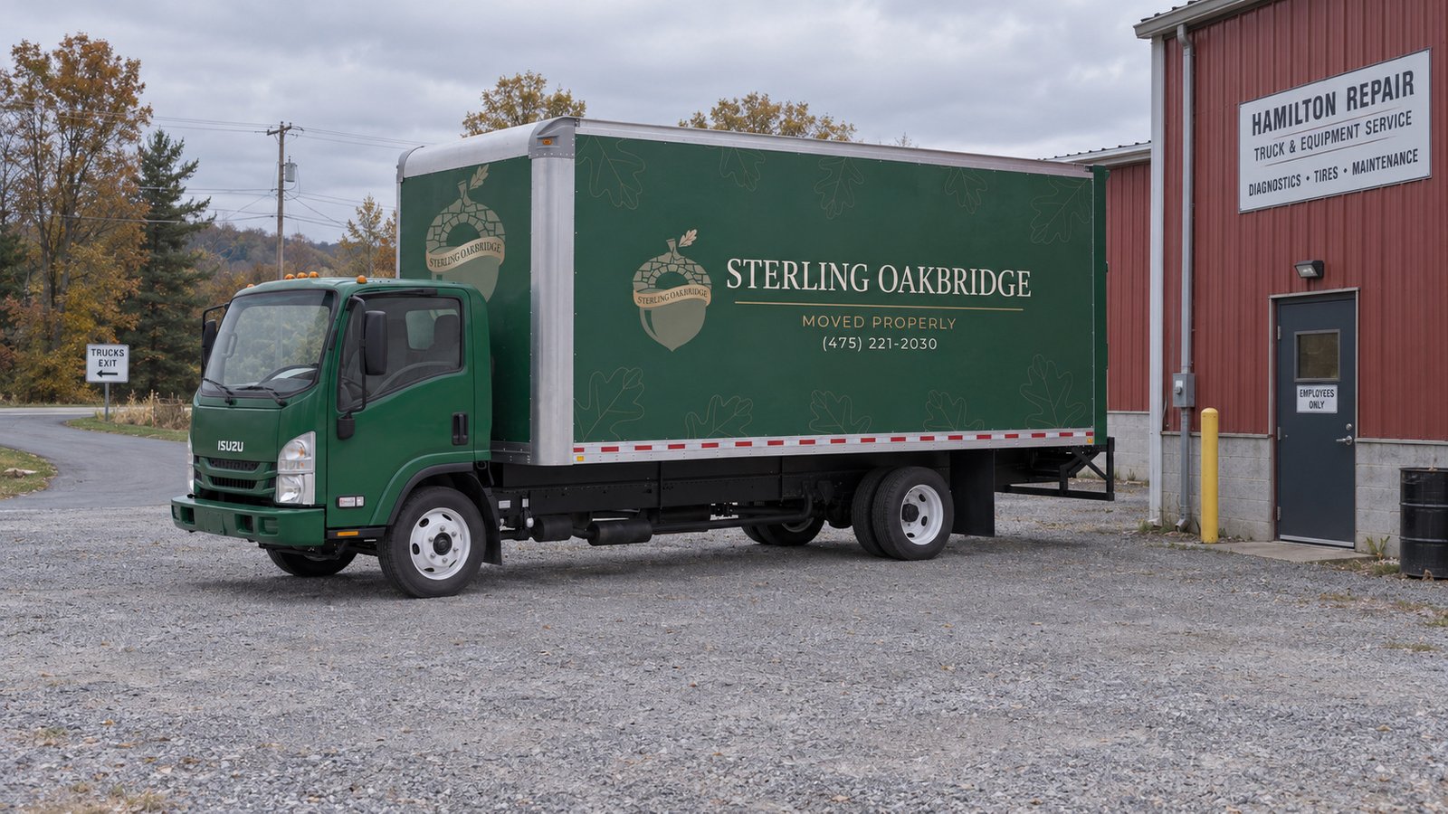 An exit and a separate entrance A complete green Sterling Oakbridge Isuzu NPR20 box truck on gravel beside a red repair workshop.