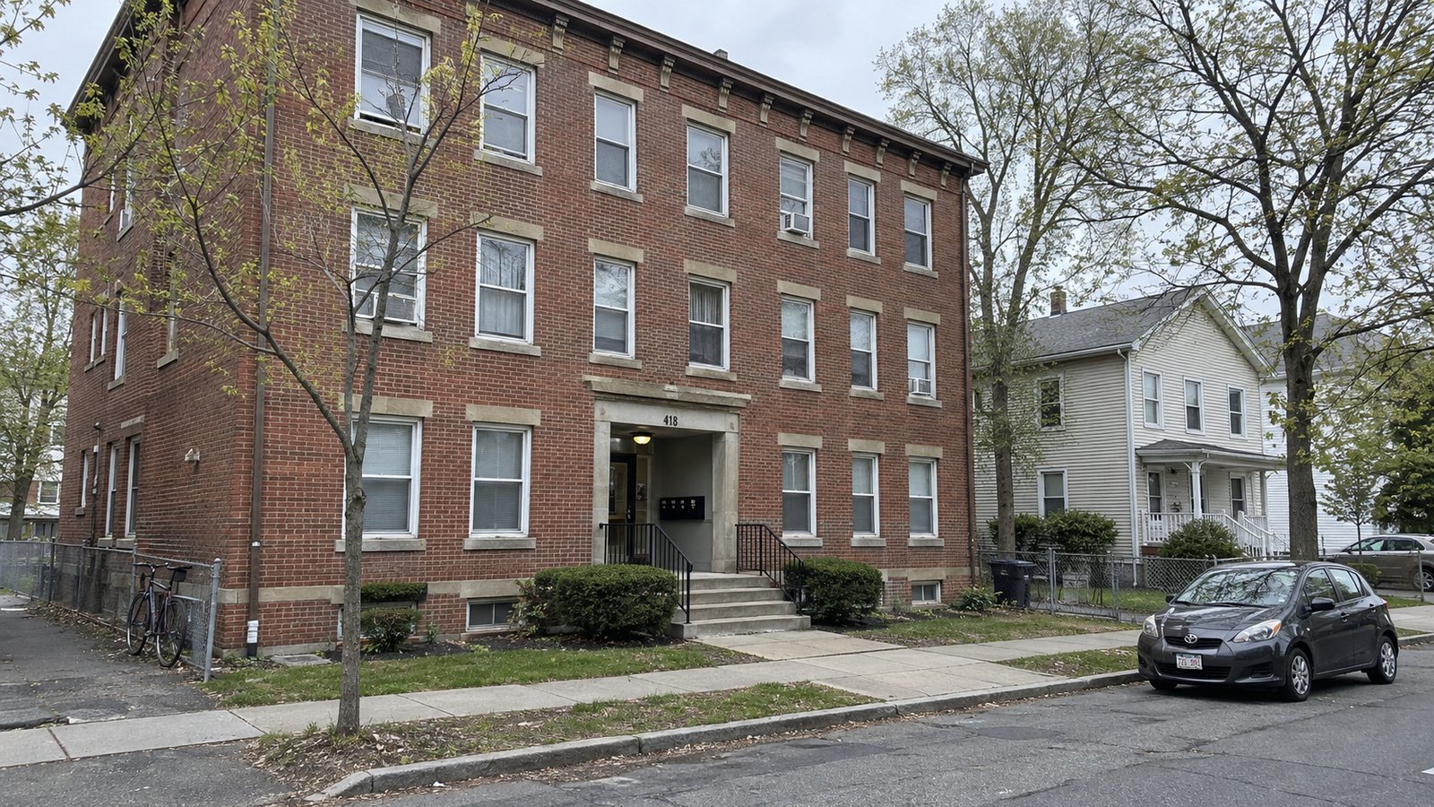 Different building types along a Springfield residential block Three-story brick apartment building with a recessed shared entrance, beside a clapboard house and residential sidewalk