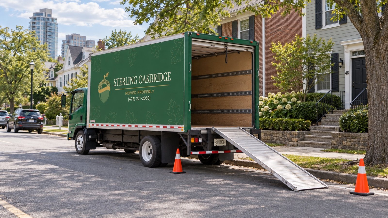 A dark green moving truck with an open rear door and a ramp resting by a residential curb.