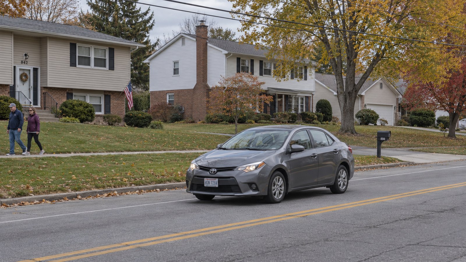 Check the outside approach A whole compact sedan on a suburban street beside two residents walking a sidewalk.