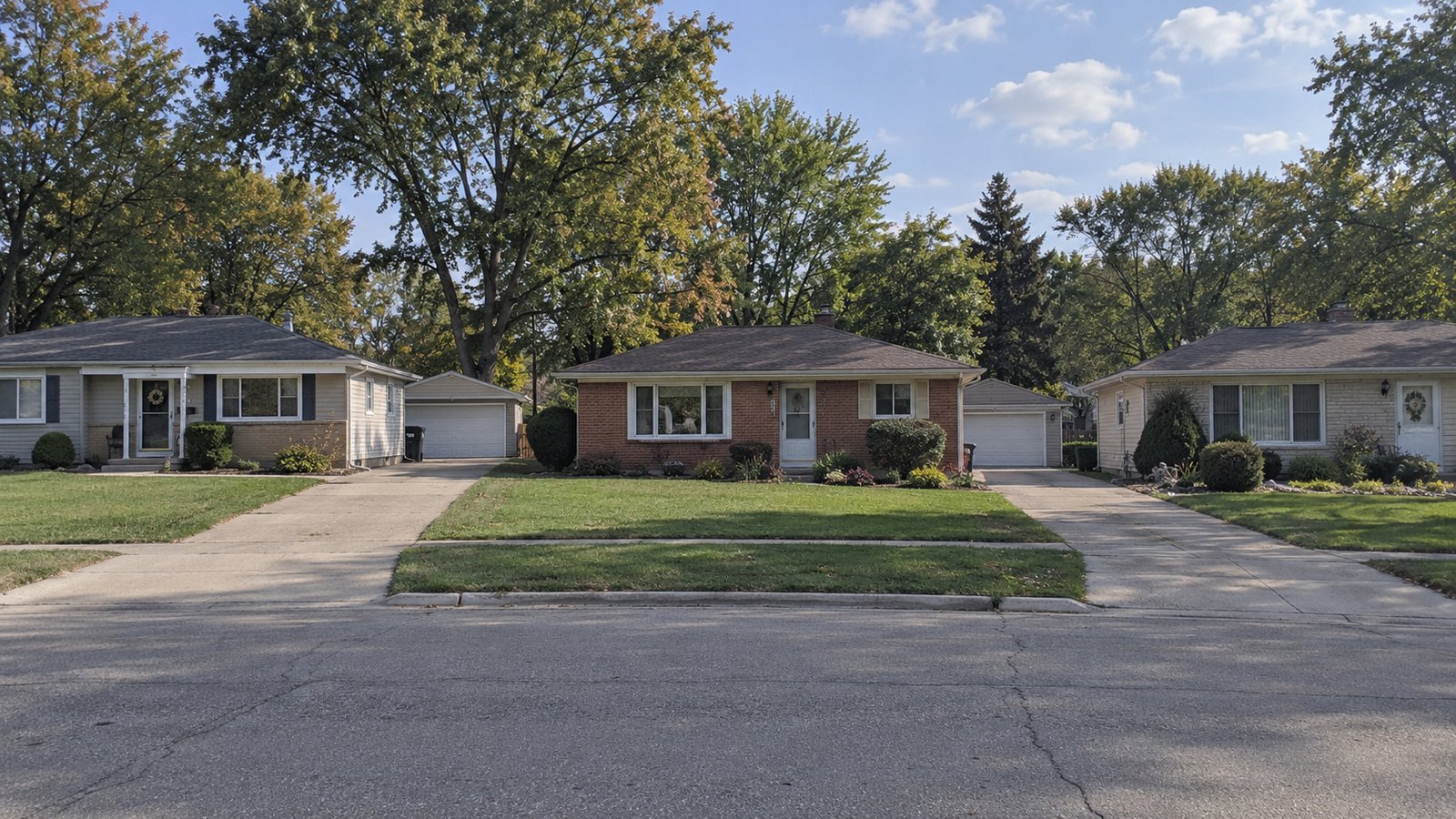 A complete brick ranch with a paved driveway beside a quiet suburban street.