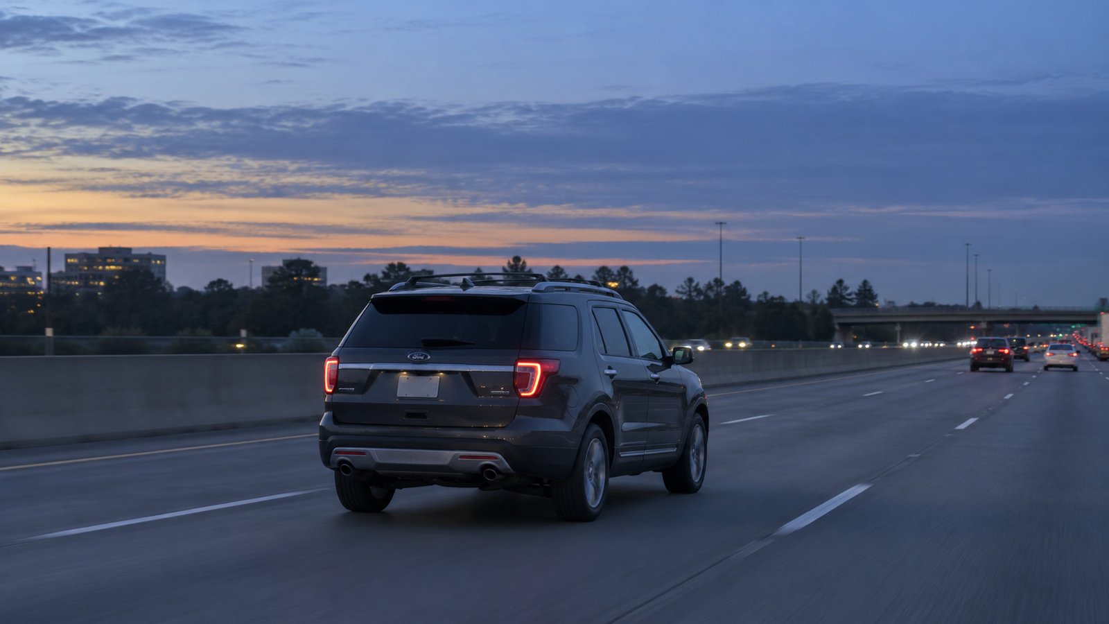 A complete gray SUV viewed from behind on a multi-lane highway at dawn.
