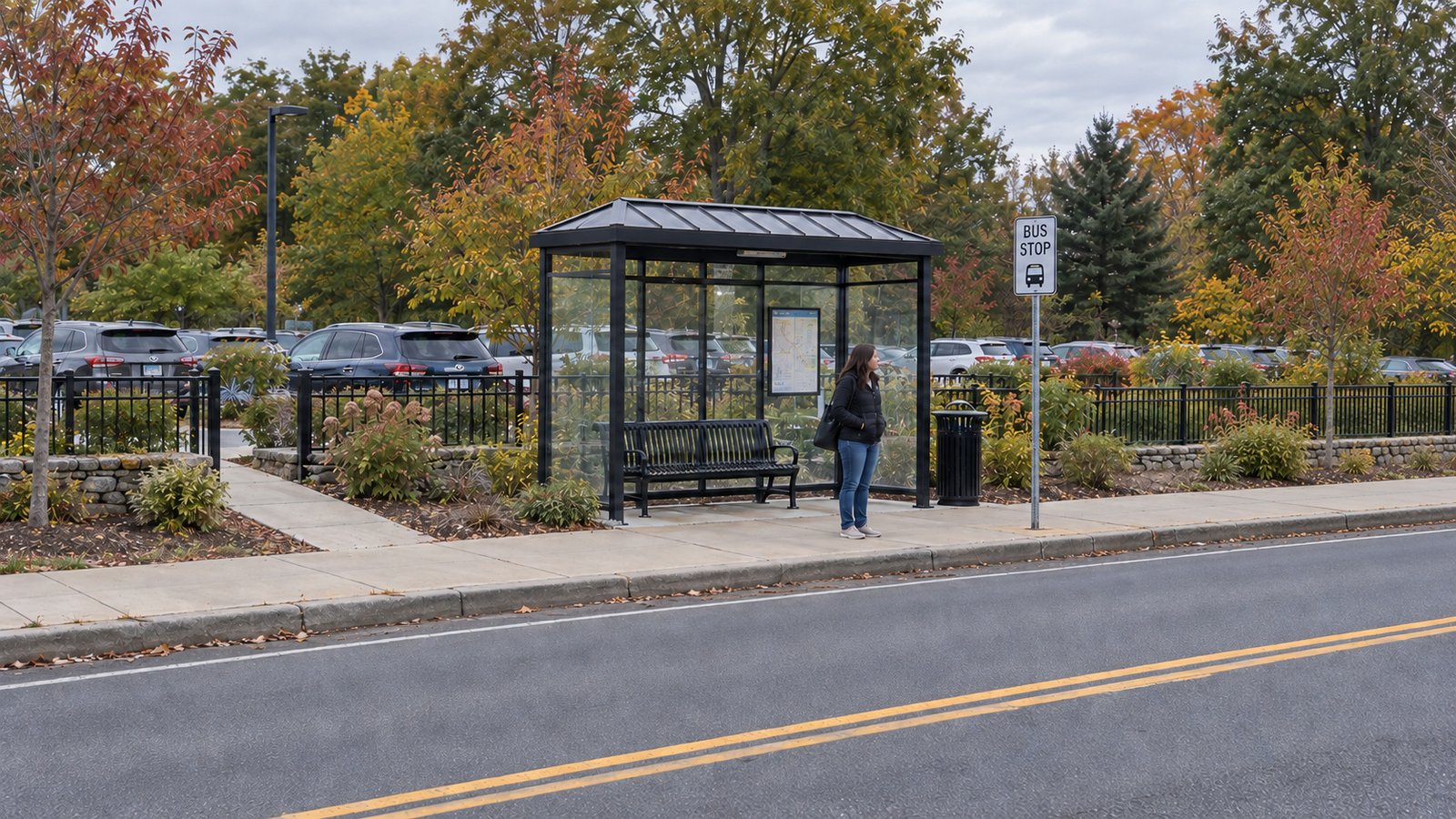 Commuter waiting at a roadside bus shelter with a separate fenced car park behind it