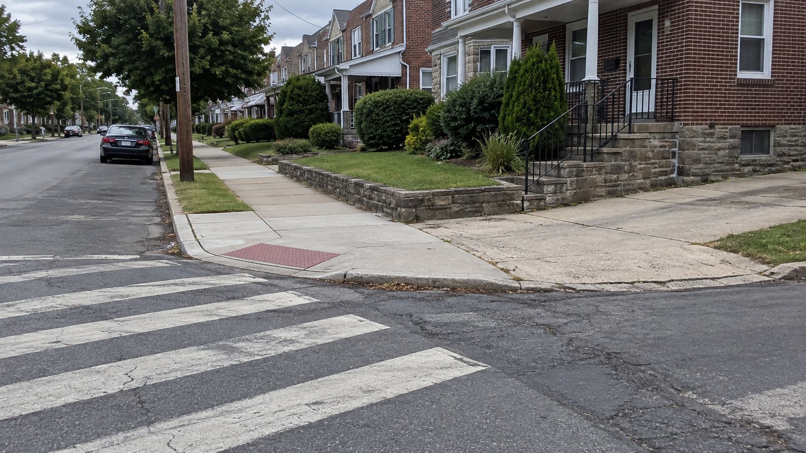 Keep the crossing separate from the working space A clear pedestrian curb ramp and painted crossing at a residential corner, with a separate driveway and curb farther along the block.