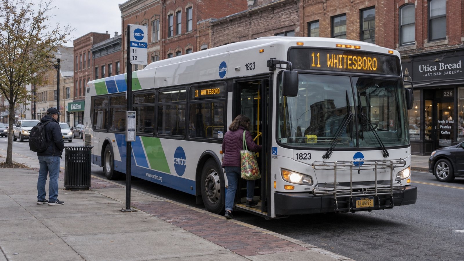 A Centro bus marked 11 WHITESBORO at a Utica sidewalk stop among older commercial buildings.