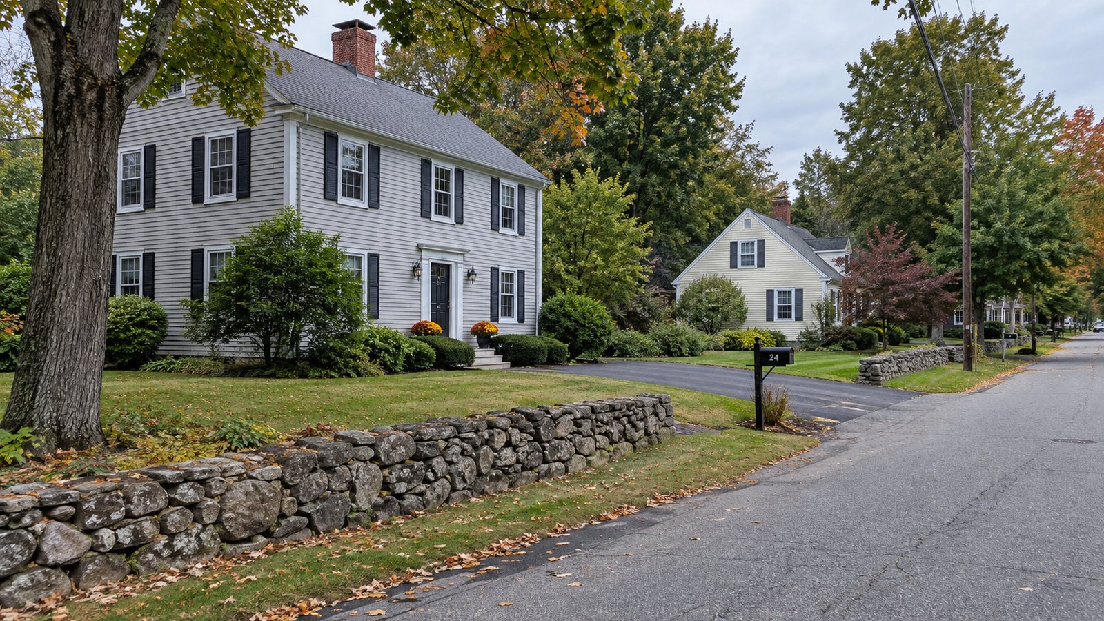 Clapboard houses, paved driveways and a low stone wall along a quiet residential street