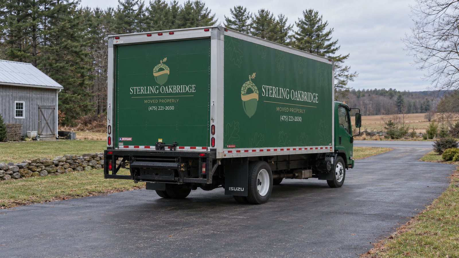 Confirm the vehicle position A whole green Sterling Oakbridge NPR16 truck seen from rear right on a paved private rural driveway beside fields.