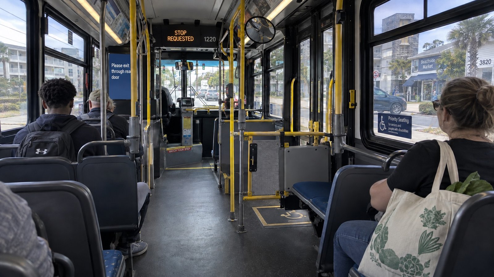 Passengers seated inside a city bus, with an open aisle, wheelchair space and a stop-requested display.