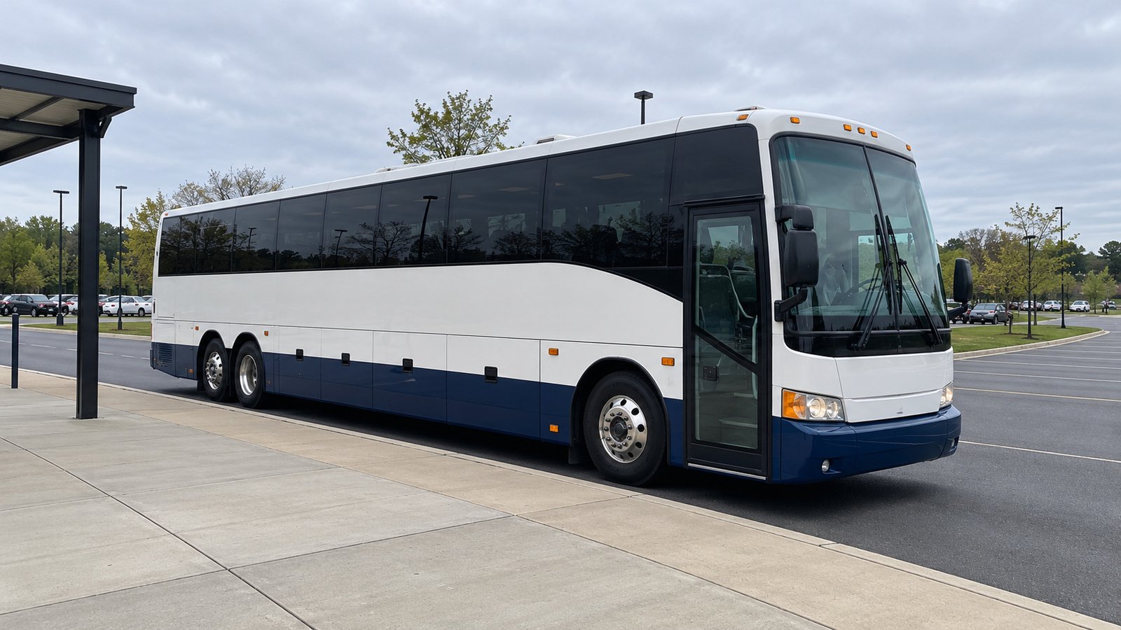 Read the boarding side and the departure lane A complete white-and-navy three-axle coach waits beside a raised platform, with its passenger door ahead of the front wheel and a clear lane beyond the nose.