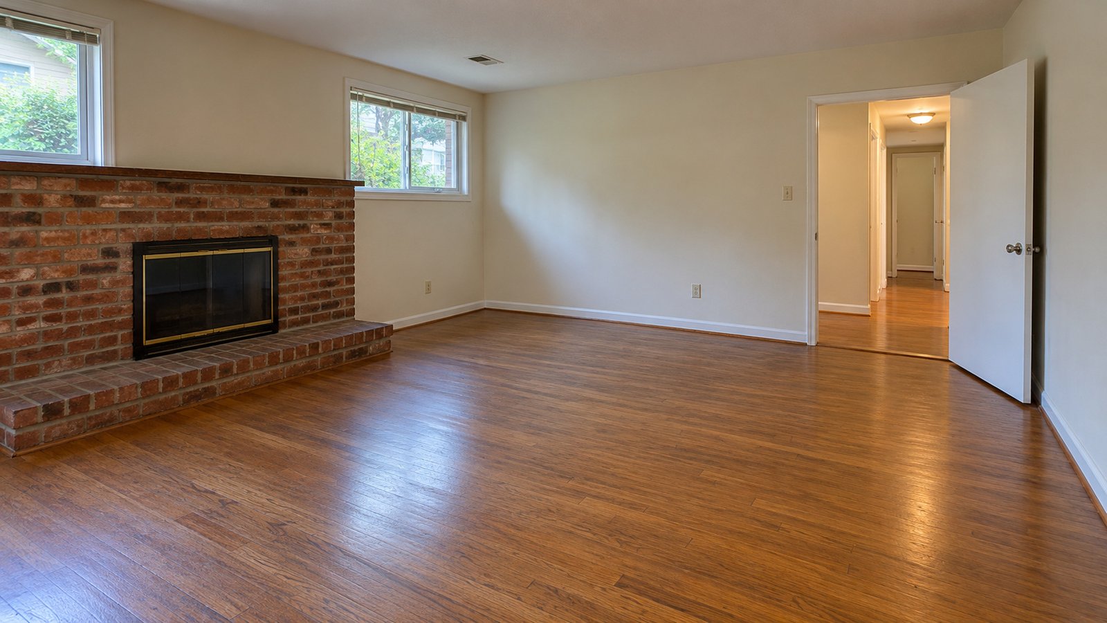 Prepare the lower-level receiving space An empty lower-level family room has an open doorway, clear wood floor and a fixed brick fireplace with a projecting hearth.