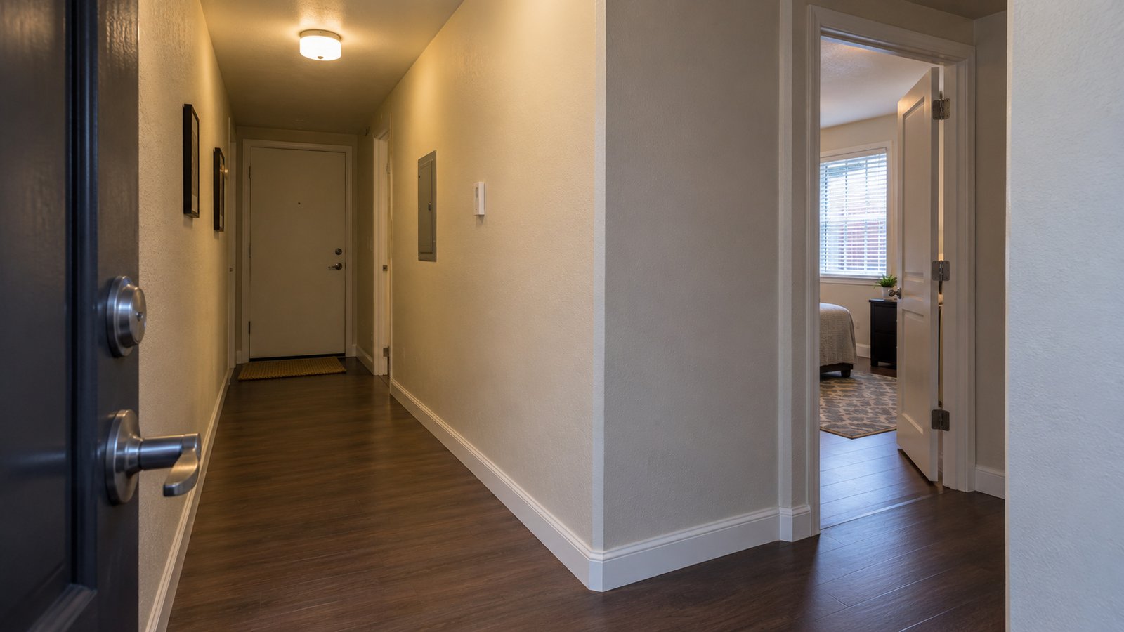 A corridor turn before the room Clear apartment hallway with a right-angle turn and an open bedroom doorway