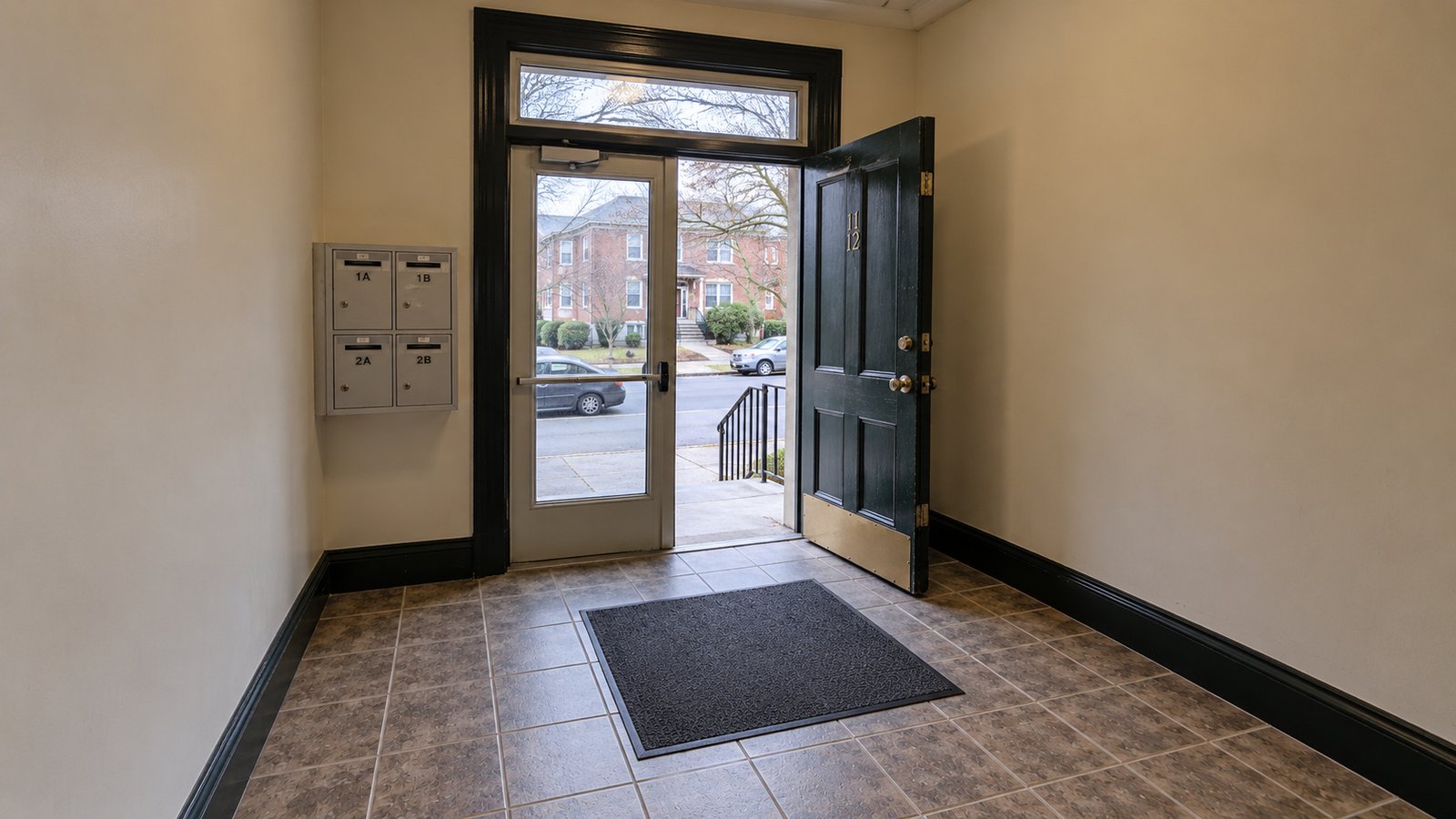 A shared entrance and the approach An apartment vestibule with an open wooden door, glazed inner door, mailbox cabinet and tiled floor.