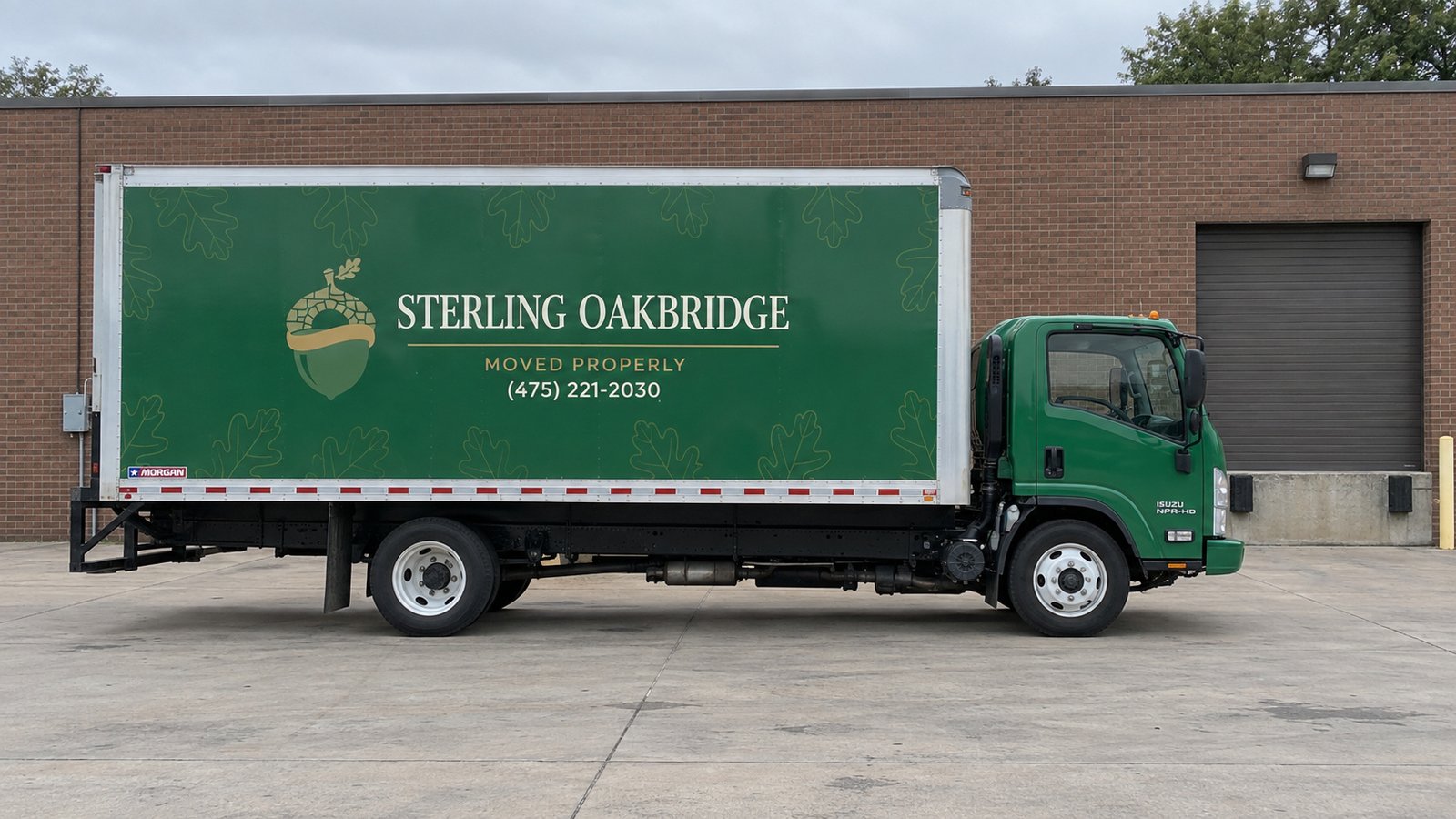 Truck position at a private receiving area A complete green Sterling Oakbridge Isuzu box truck parked beside a brick wall on a private paved receiving apron.