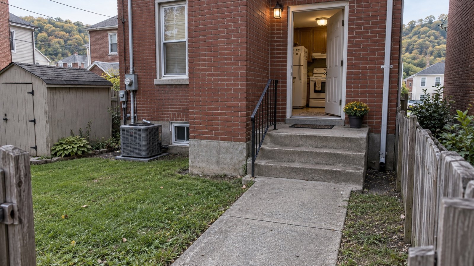 Concrete rear courtyard leading to three broad steps, a handrail and an open kitchen door