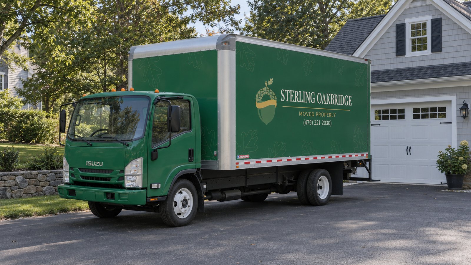 A proposed private standing point A complete green Sterling Oakbridge Isuzu NPR box truck on a paved private driveway beside a garage.