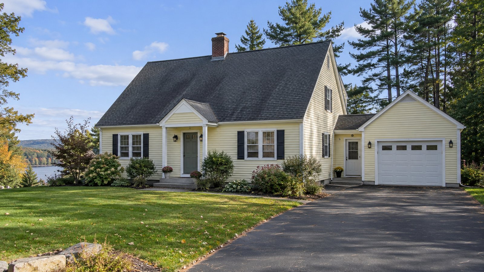 A home and its arrival route A complete pale yellow cape house and attached garage beside a paved driveway and tall trees.