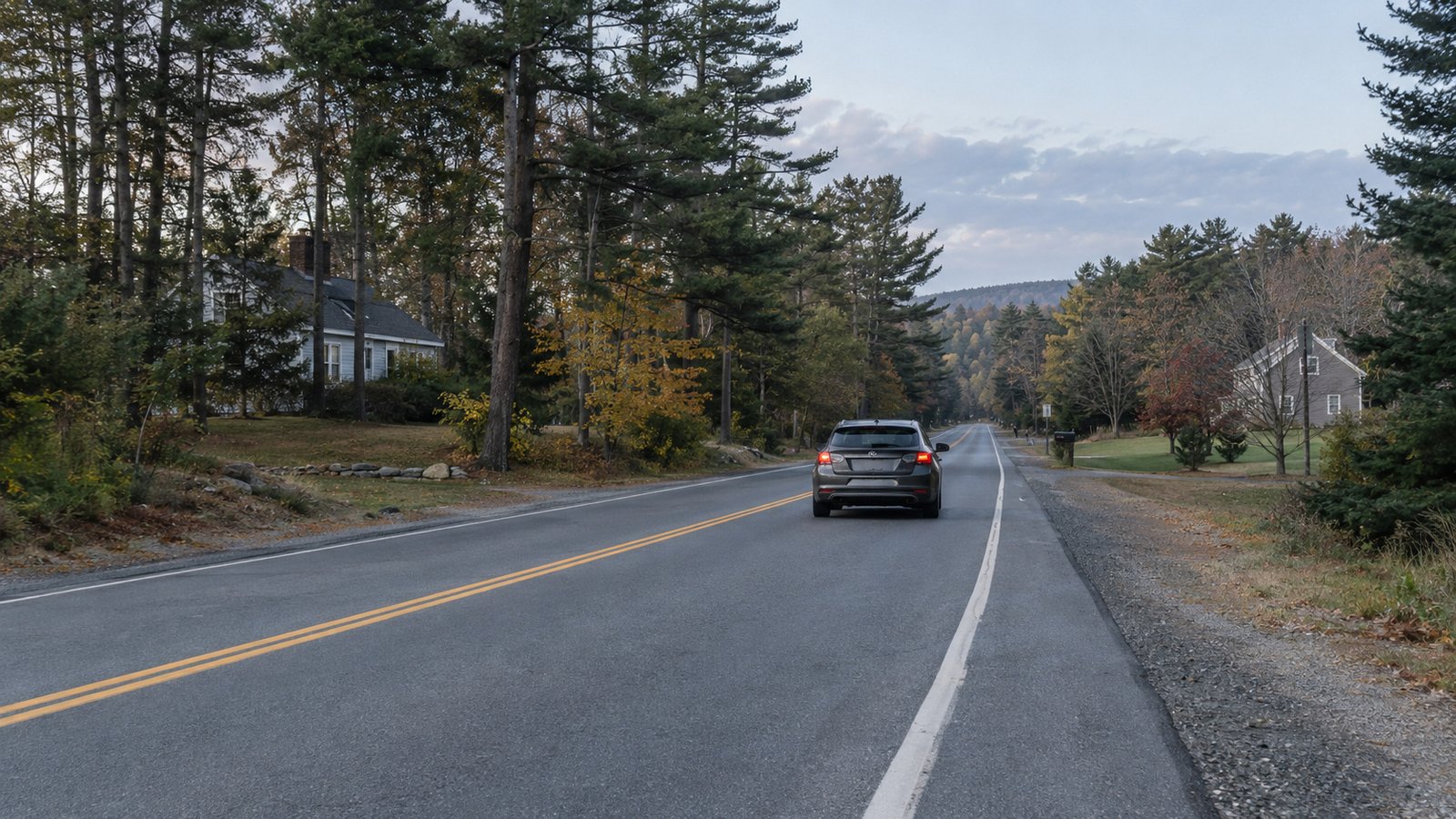 The whole rear of a compact car traveling away in the right lane of a two-lane inland Maine road.
