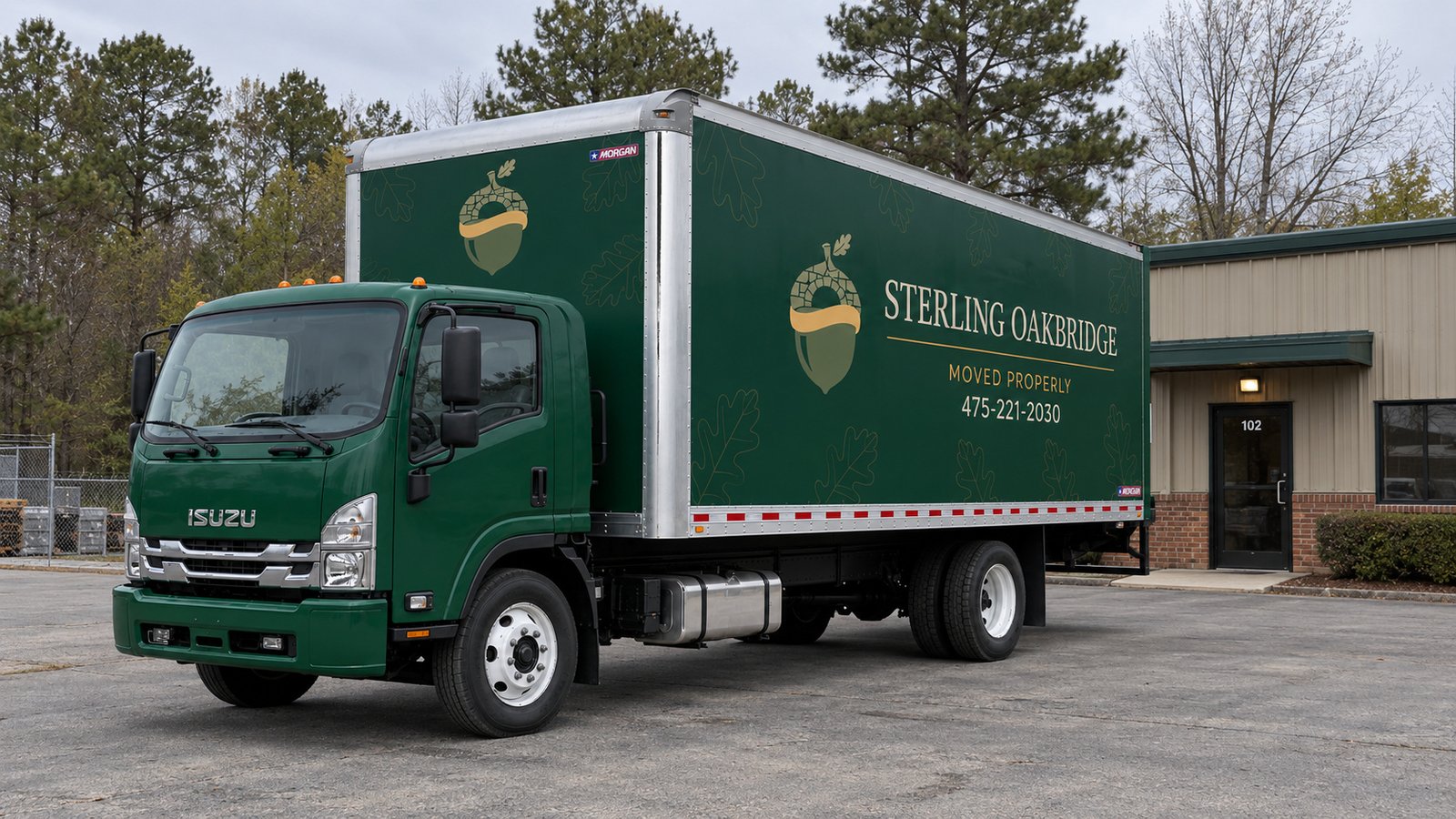 Green Sterling Oakbridge Isuzu FTR box truck parked on a private paved apron beside a low building