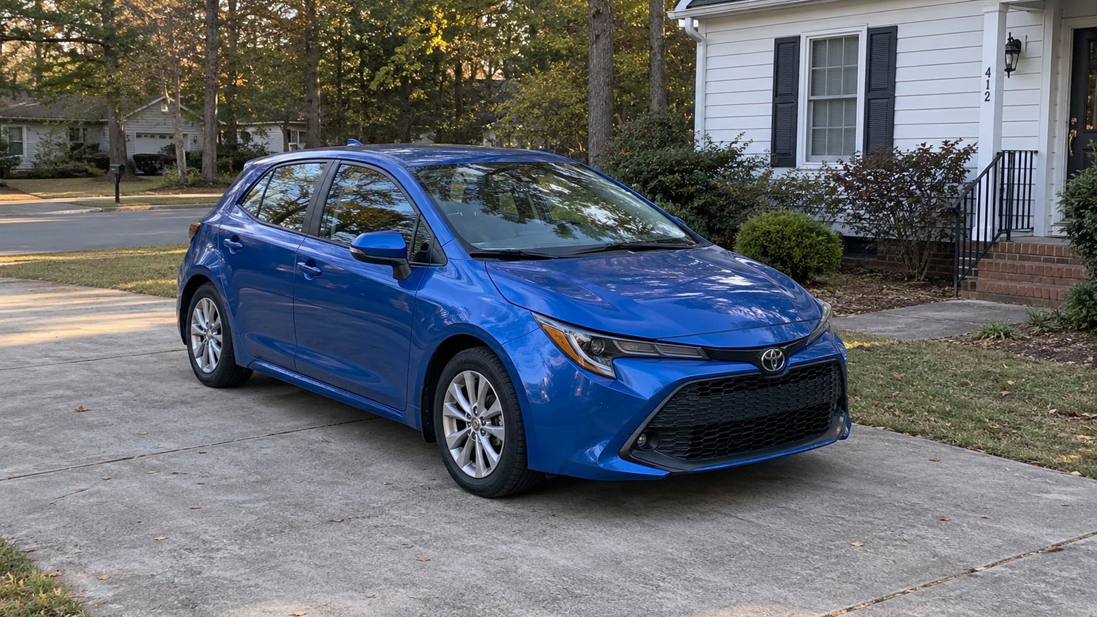 Blue compact hatchback parked on a private paved driveway beside a modest home