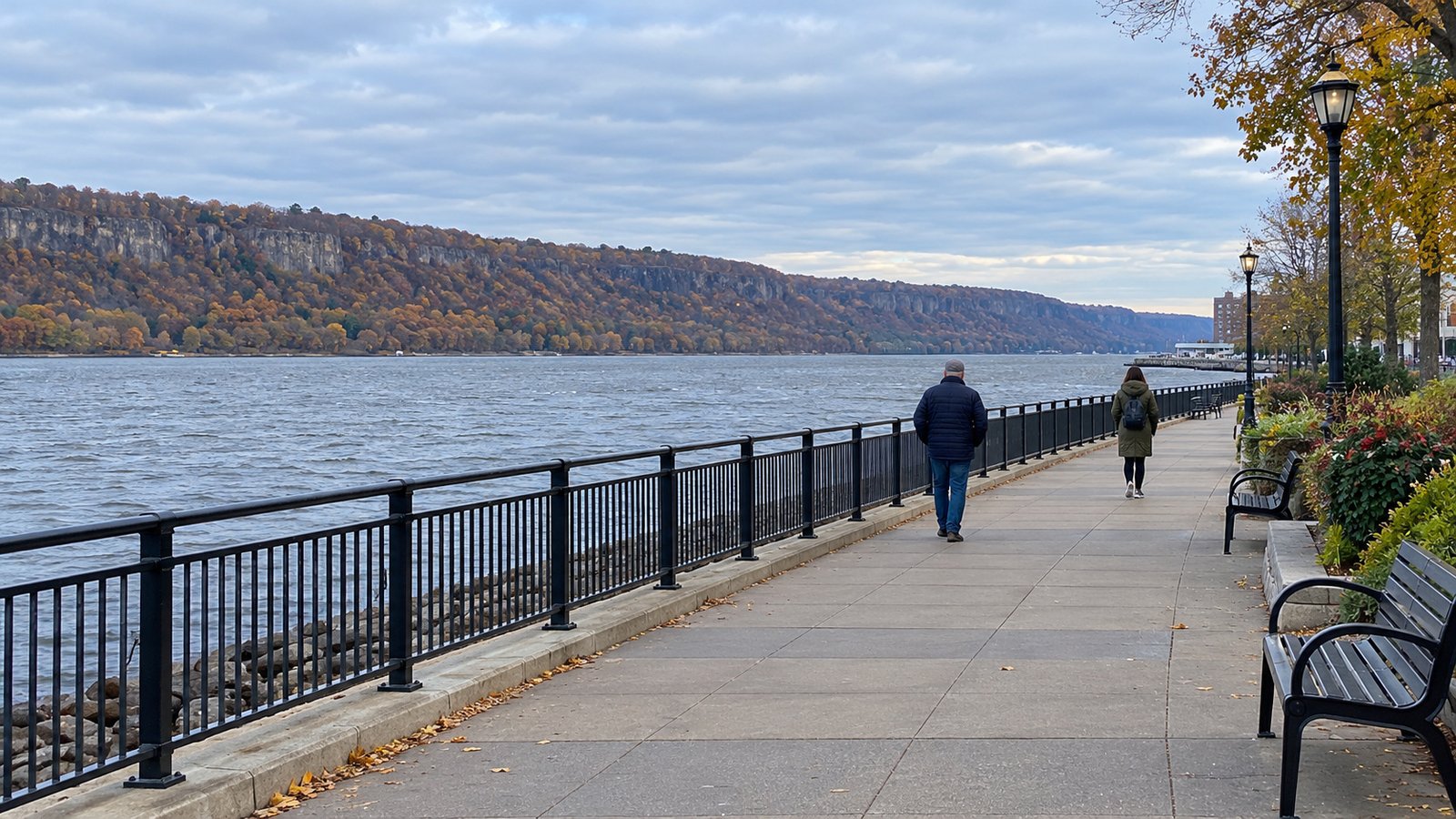 The Hudson waterfront Pedestrians on a riverside promenade facing a wooded bluff across the Hudson.