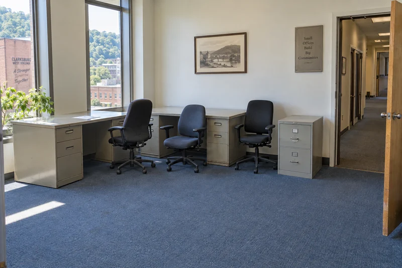 Two empty pedestal desks, used swivel chairs and a short filing cabinet arranged in an older office with a clear exit route