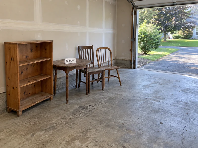 A worn bookcase, occasional table and two spare chairs grouped beside an open garage route A used bookcase, small table and two spare chairs grouped for removal beside a clear garage route
