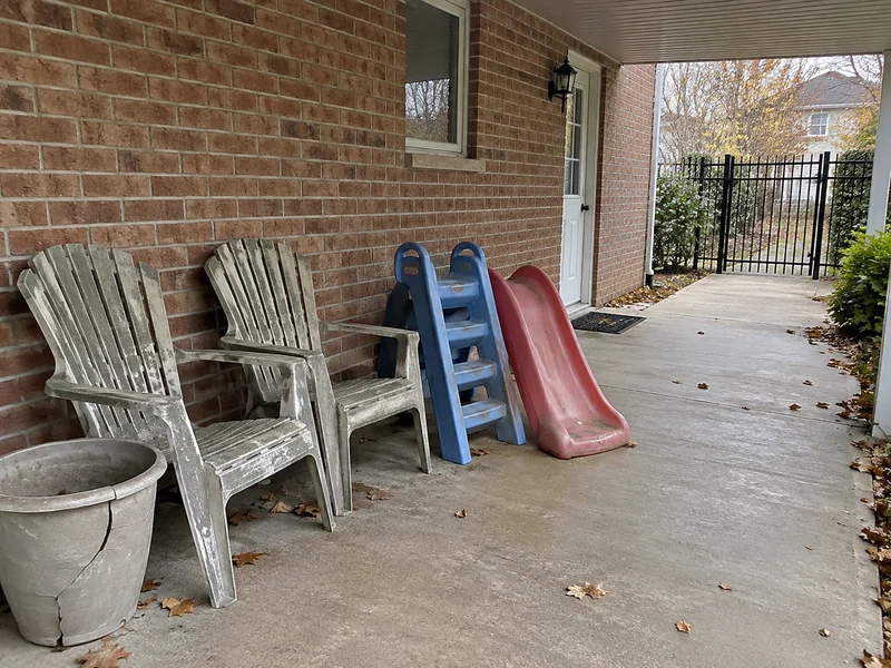 Weathered patio chairs, separated small slide pieces and an empty planter beside a clear covered path